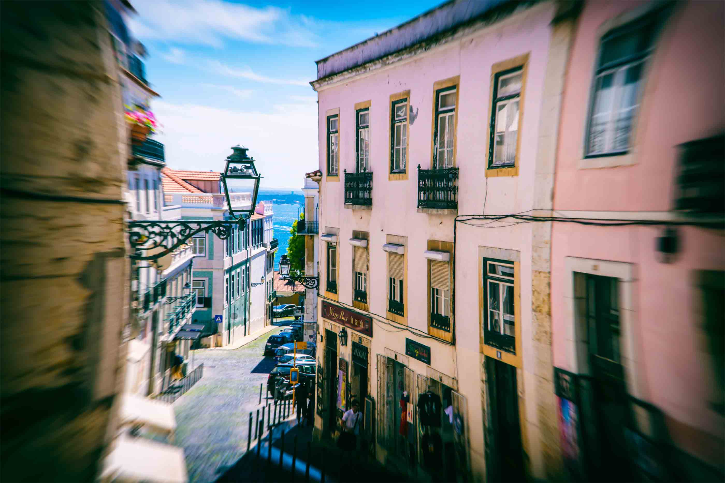 Rua em Lisboa, entre prédios, que desce em direção ao rio.