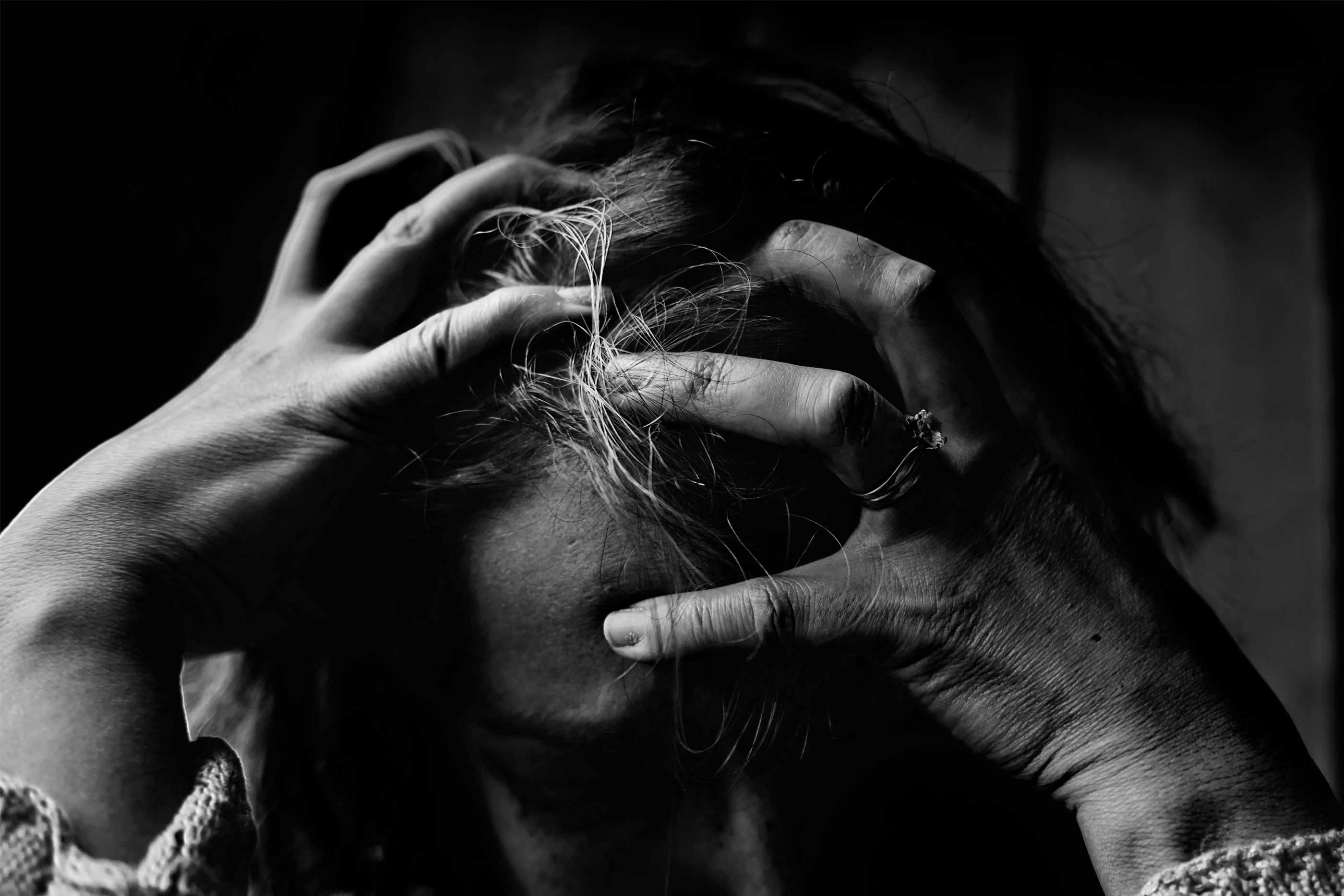Imagem a preto e branco mostra uma mulher com as mãos na cabeça e a ter um esgotamento nervoso. Está em lágrimas e quase a arrancar os cabelos.