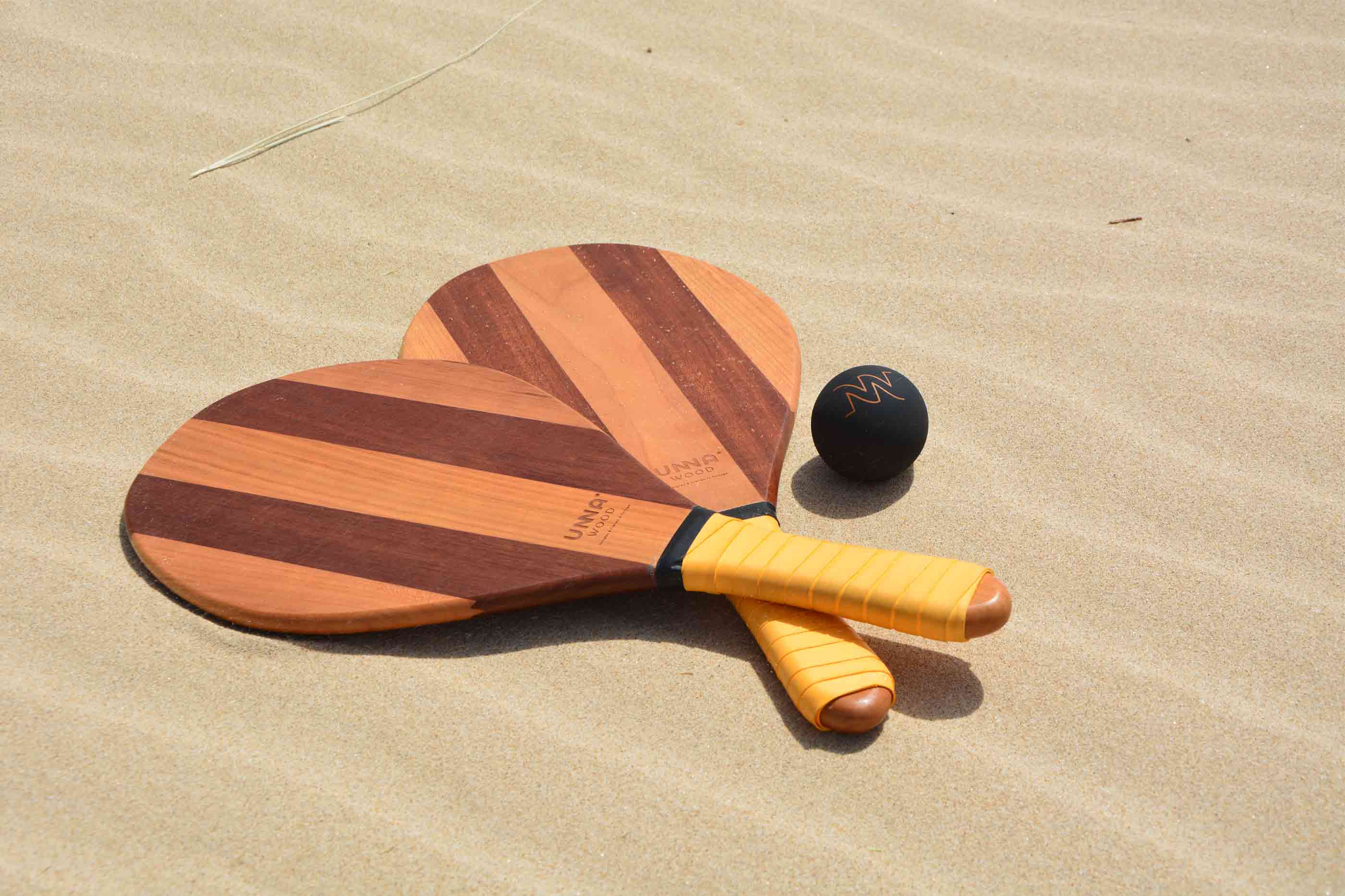 Duas raquetes de praia e uma bola preta na areia