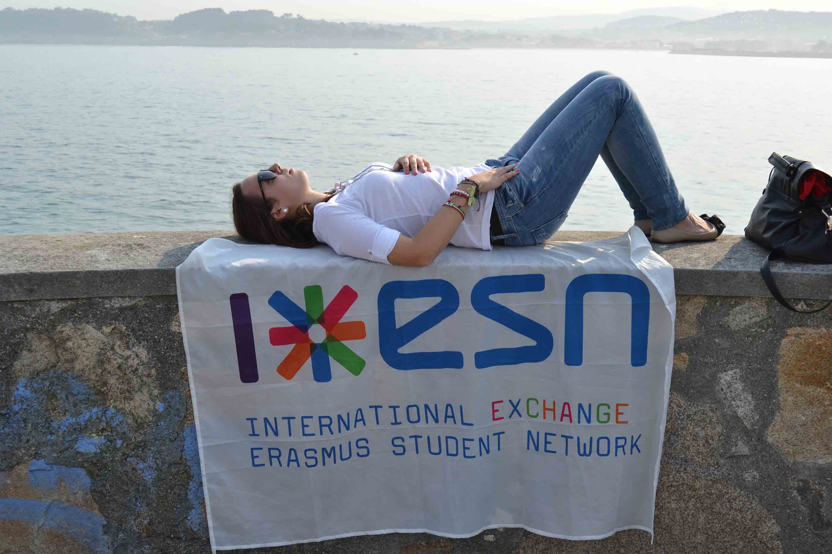Rapariga a descansar deitada à beira rio em cima de um muro e da bandeira da ESN