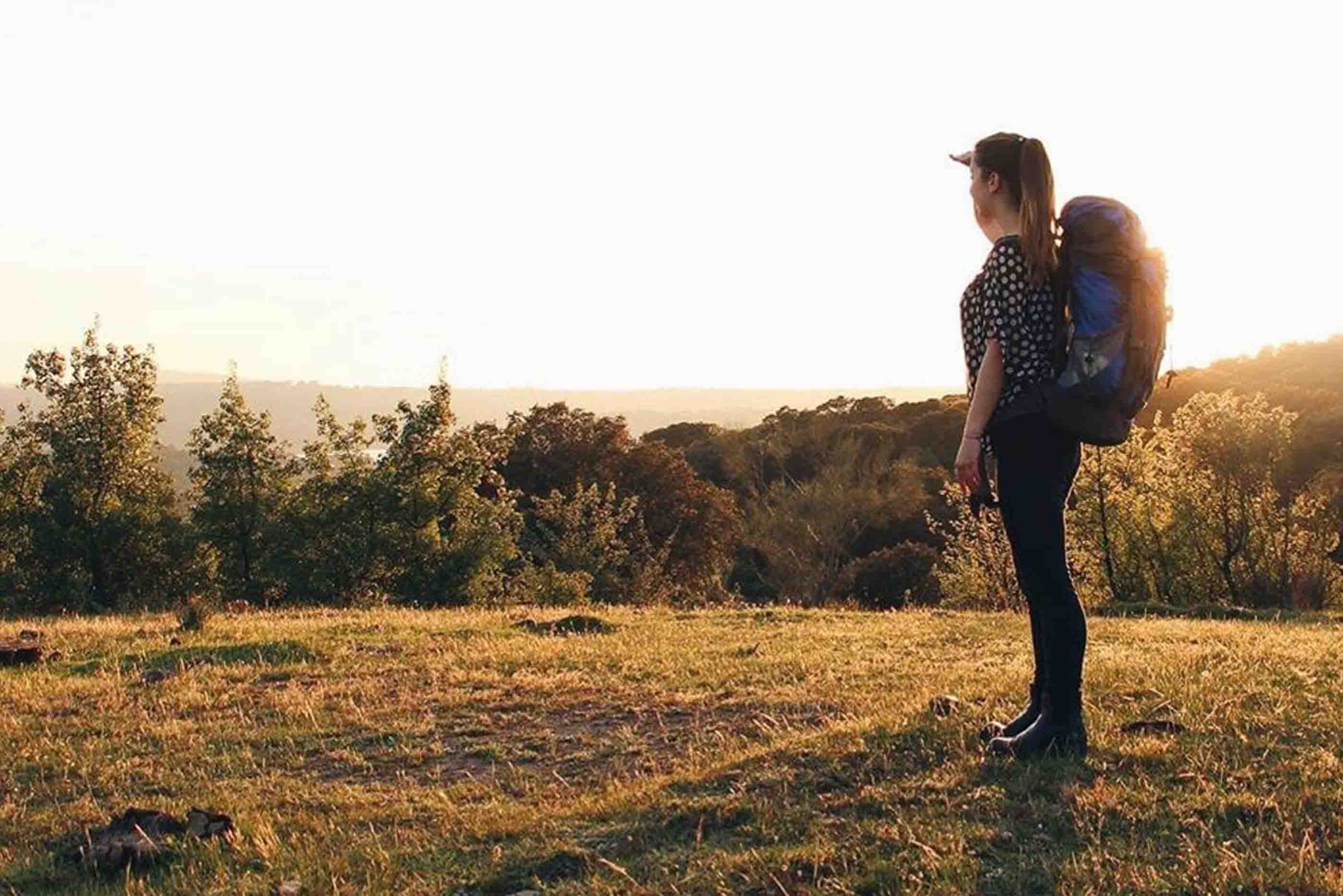 Rapariga com mochila de campismo às costas a olhar para a paisagem