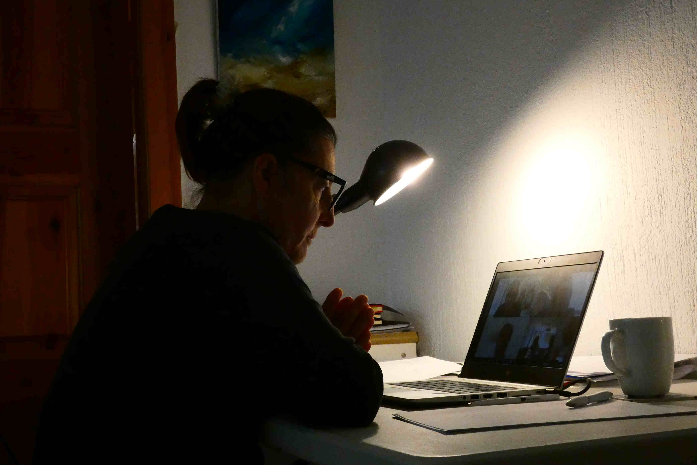 Mulher sentada à secretária a participar numa videoconferência por meio do portátil.