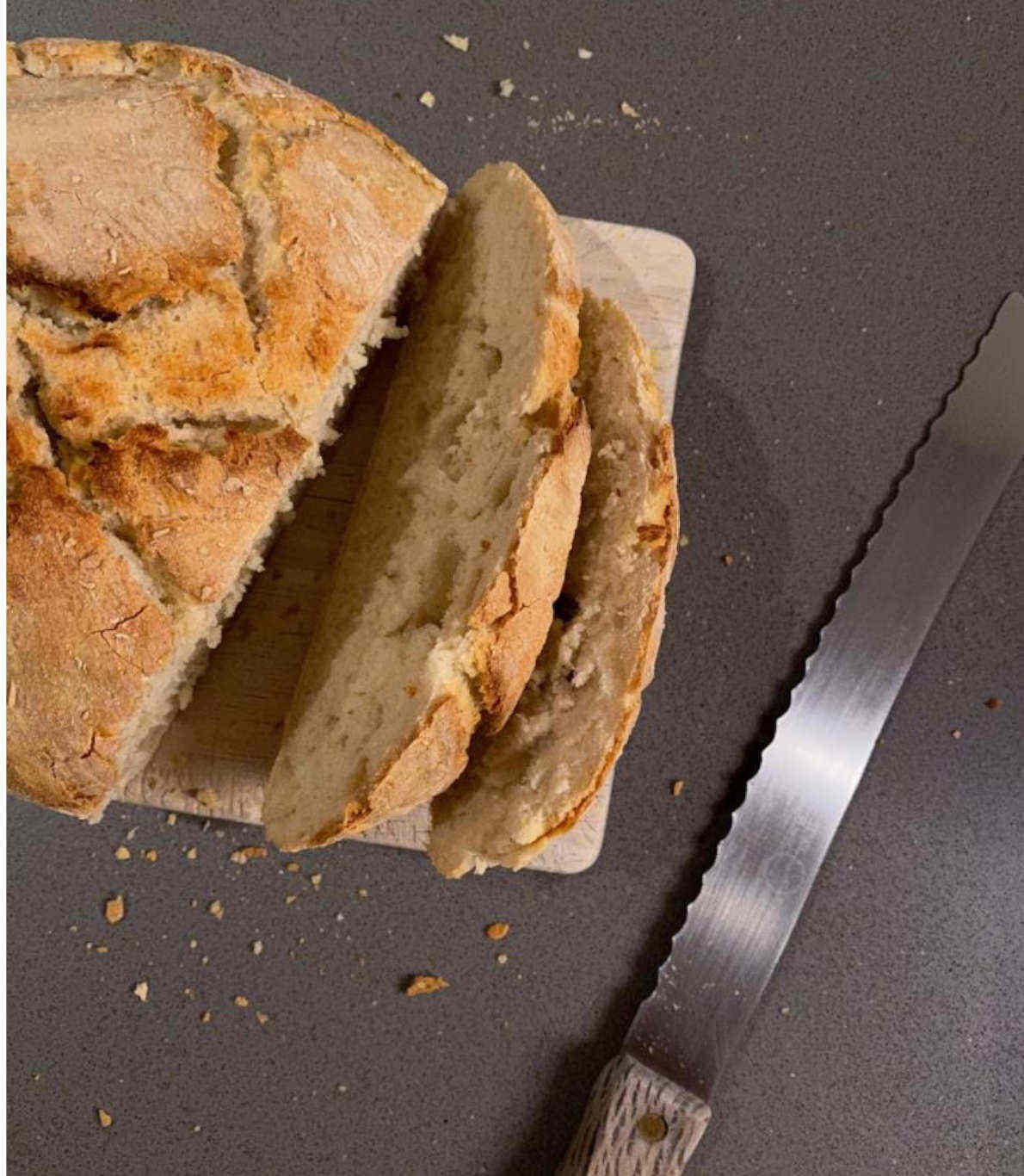 Pão caseiro, cortado às fatias, num tabuleiro com faca de serrilha ao lado.