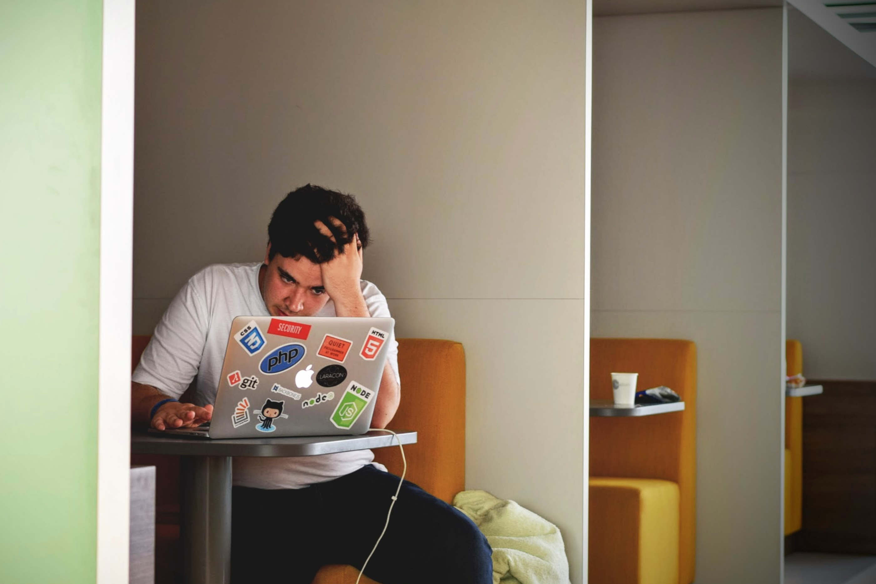 Rapaz sentado em frente ao computador, com a mão na cabeça, demonstrando algum stress e preocupação.
