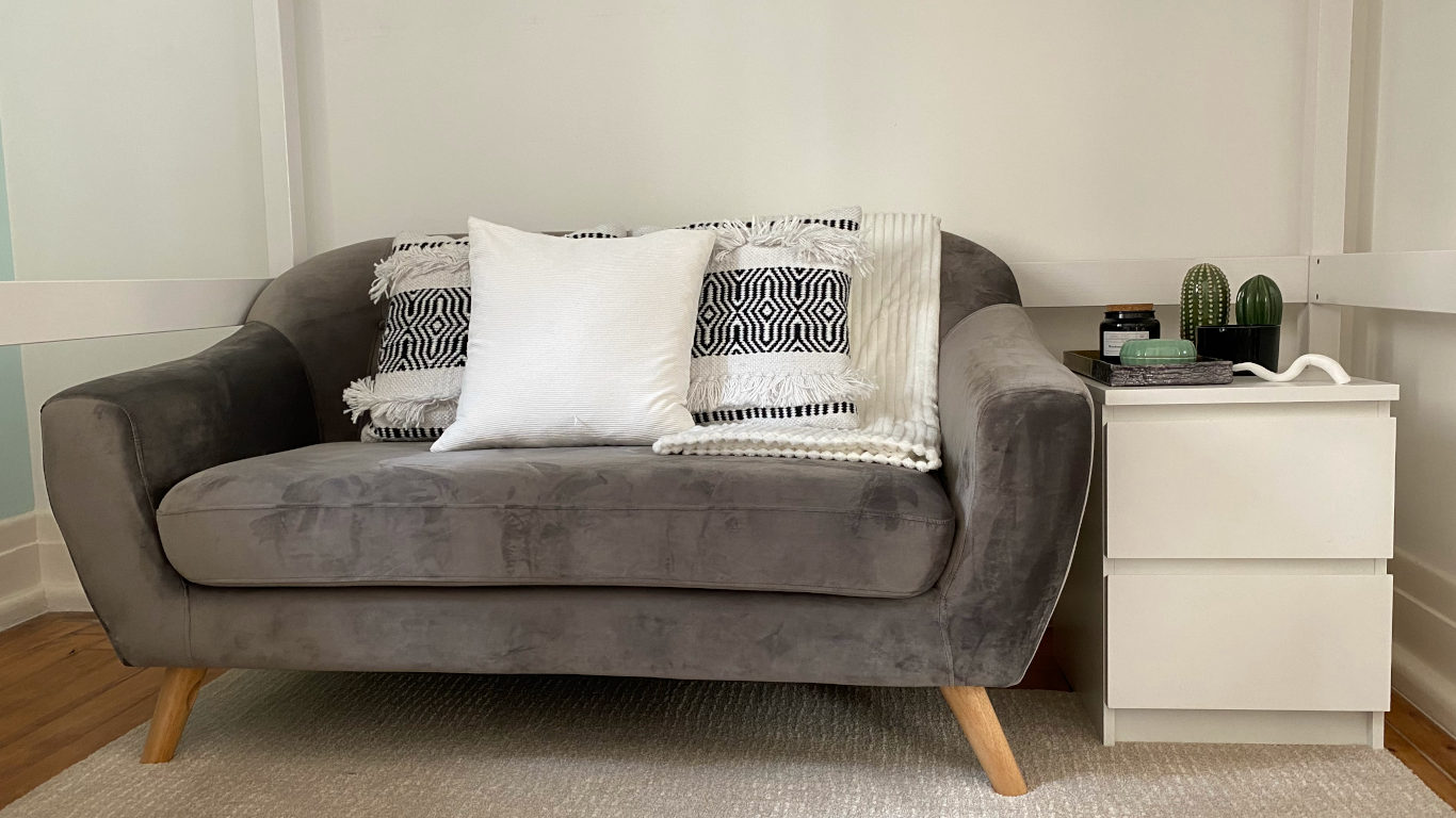 Espaço confortável com um sofá de veludo cinzento revestido de almofadas e uma manta brancas