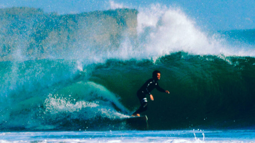 Surfista a surfar uma onda com um fato de surf preto