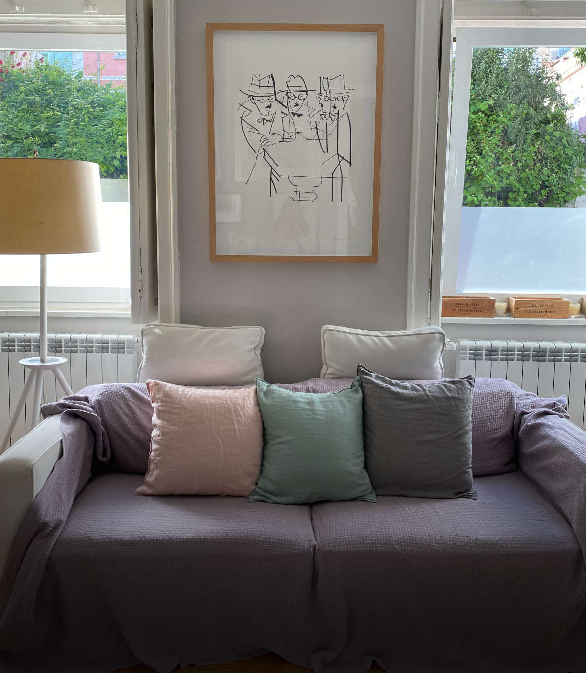 Canto de uma sala de estar com um sofá branco revestido de almofadas coloridas e uma manta lilás por cima