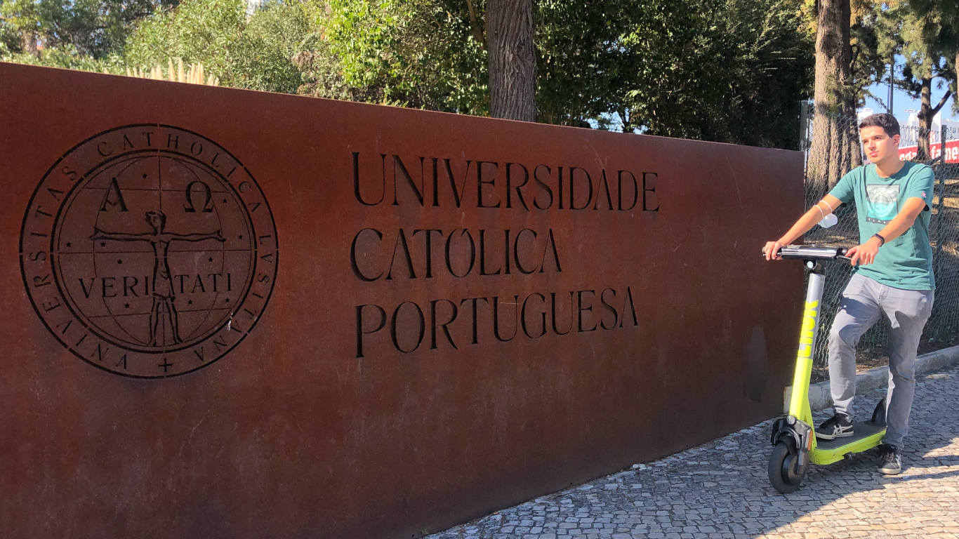 Aluno da Universidade Católica Portuguesa junto de uma trotinete na entrada da faculdade