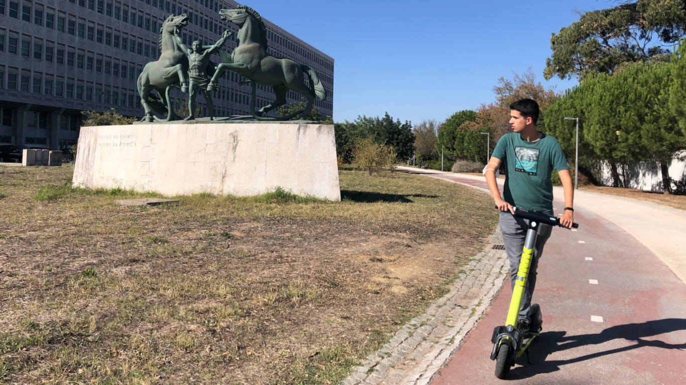 Aluno da UCP em cima da trotineta a olhar para a estátua com dois cavalos do Estabelecimento Prisional de Lisboa