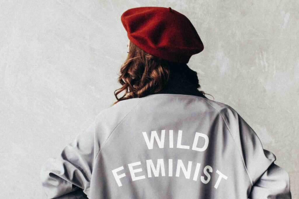 rapariga de costas com boina vermelha e casaco cinzento a dizer wild feminist