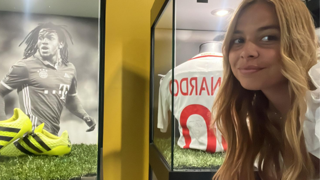 Rapariga posa à frente de uma vitrine com camisola de ex jogador.