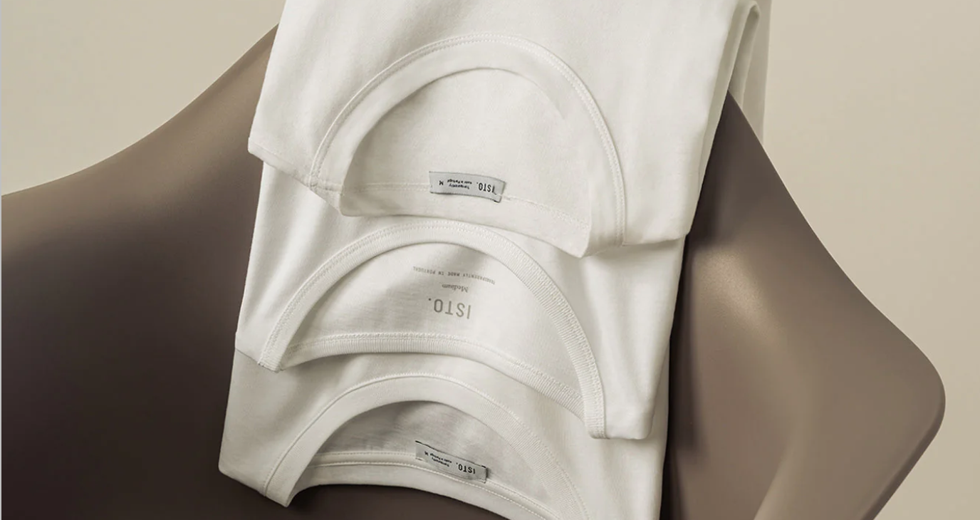 Camisolas brancas da marca ISTO. dobradas e colocadas numa cadeira cinzenta.