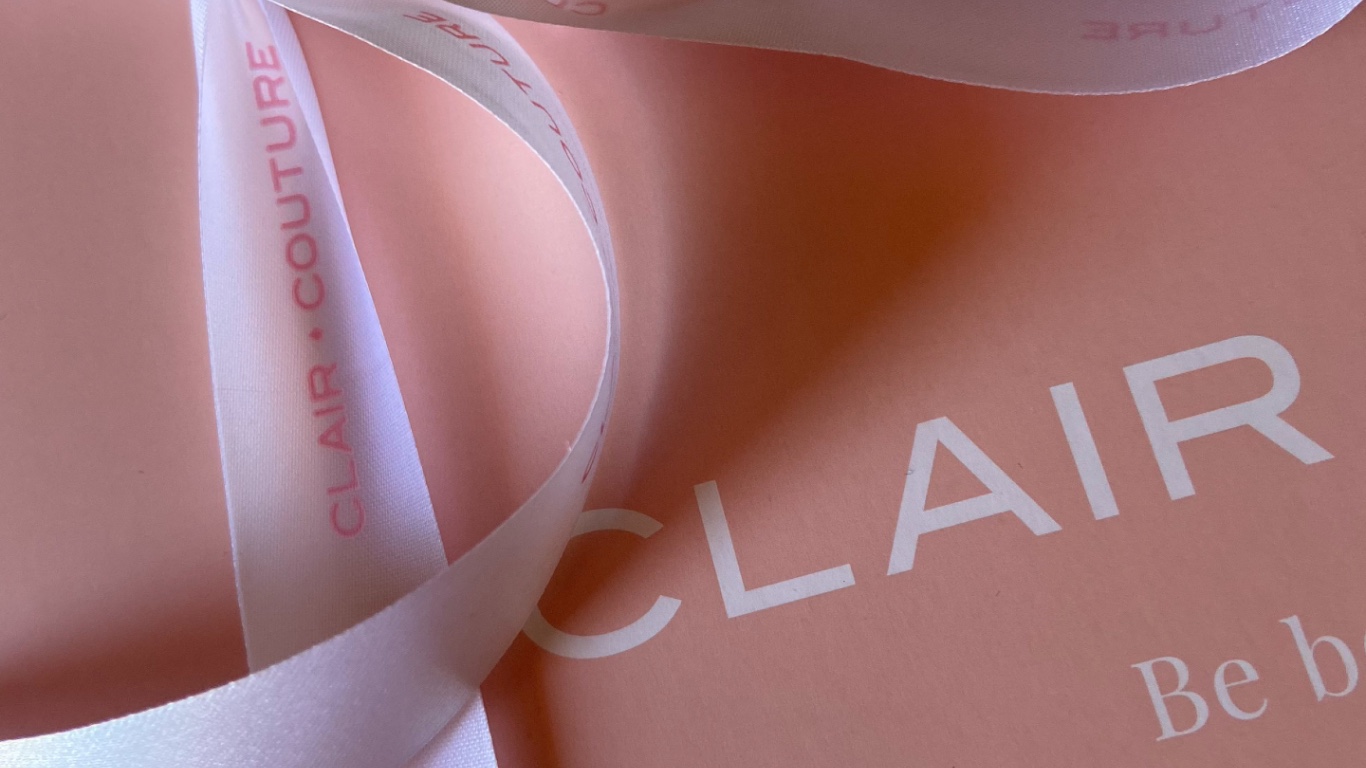 caixa de presente cor de rosa da Clair Couture com o nome da marca e um laço branco