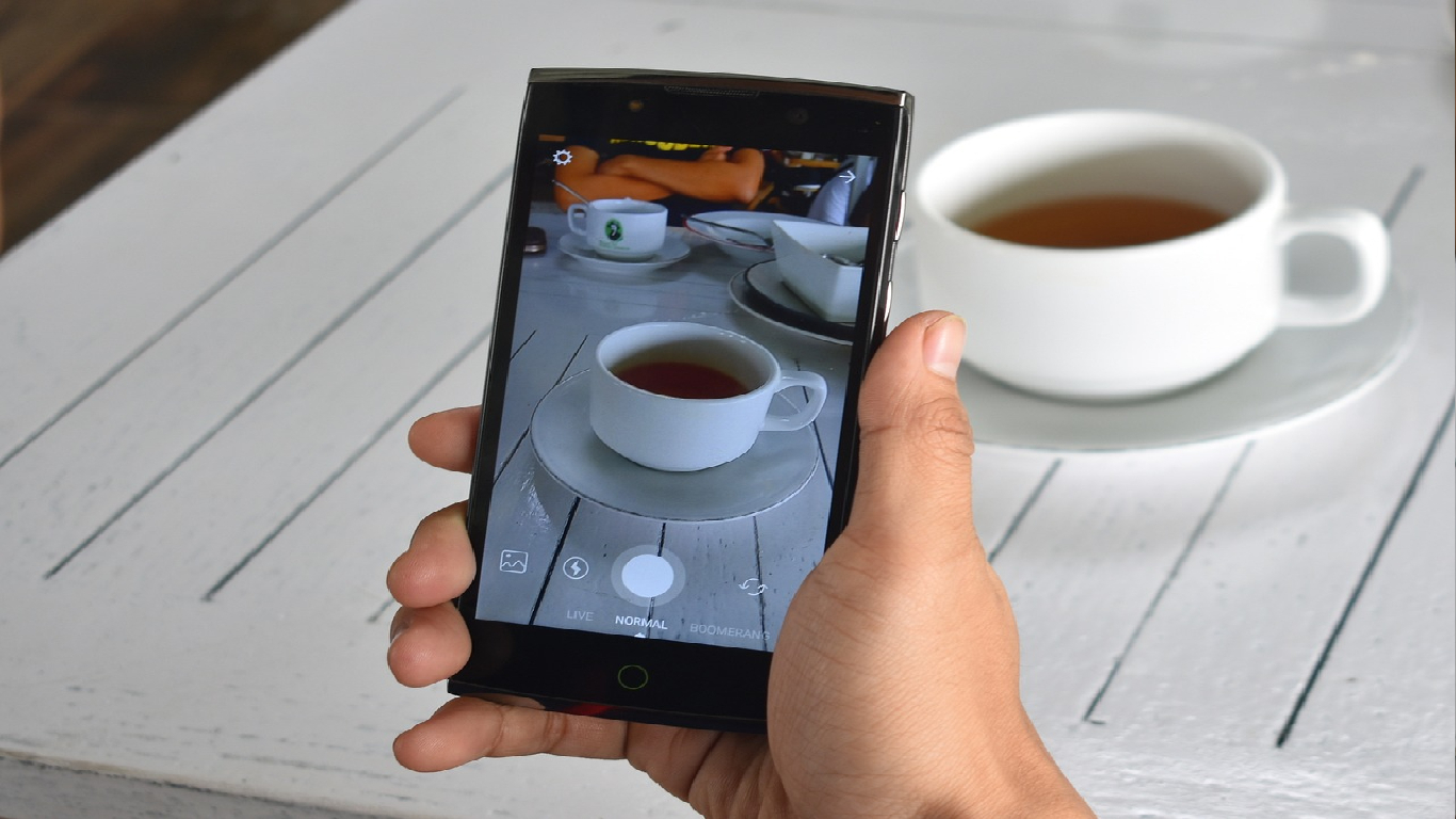Um indivíduo a editar uma chávena de café com seu telemóvel.