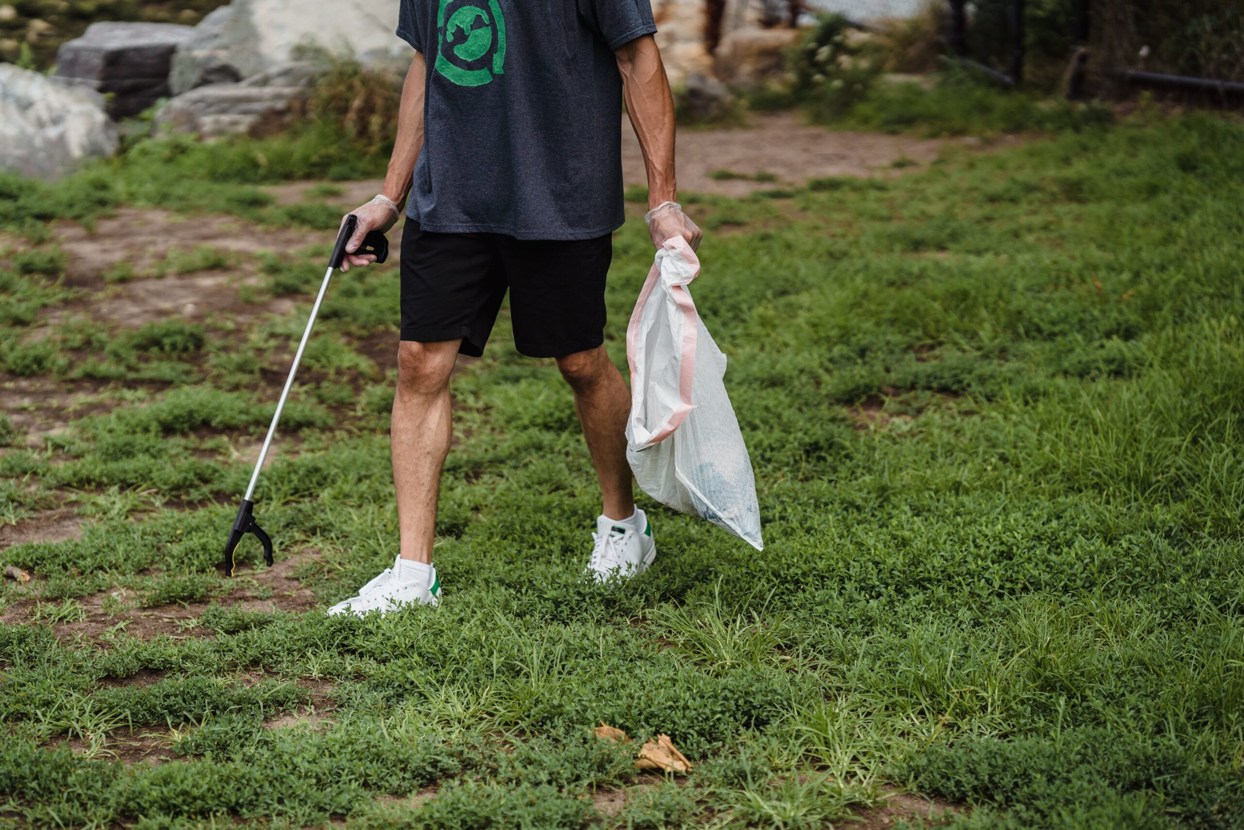 Homem de calções e t-shirt a apanhar lixo de uma relva
