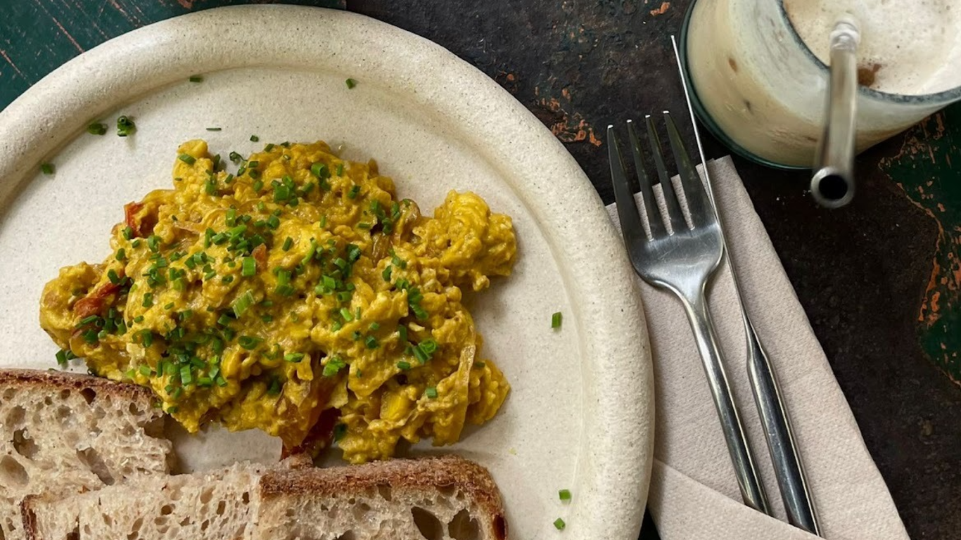 Prato de ovos mexidos num tom mais amarelo, servidos num prato simples com pão