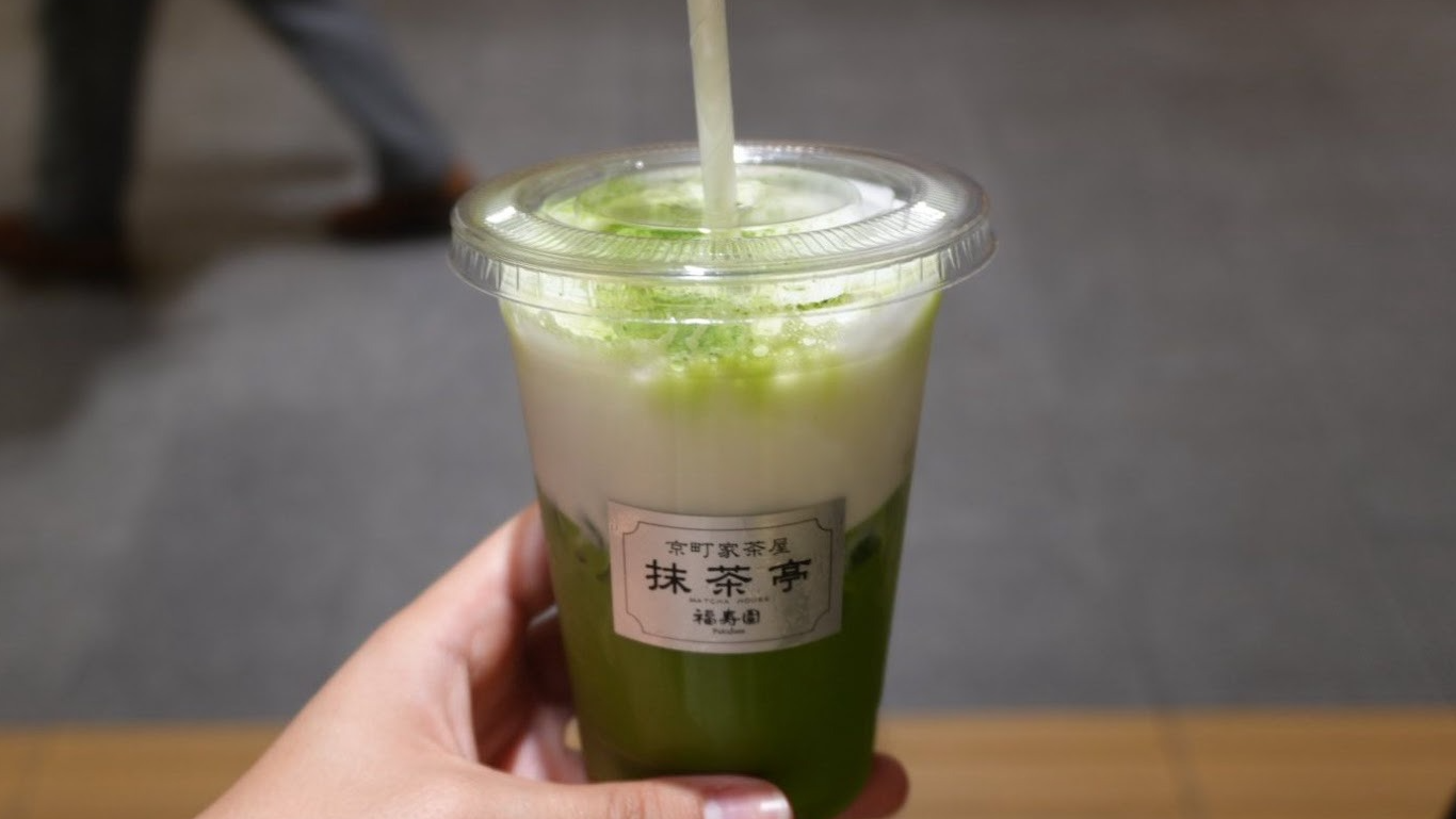 Copo transparente com chá matcha. A bebida tem camadas de cor verde e, na superfície, branca.
