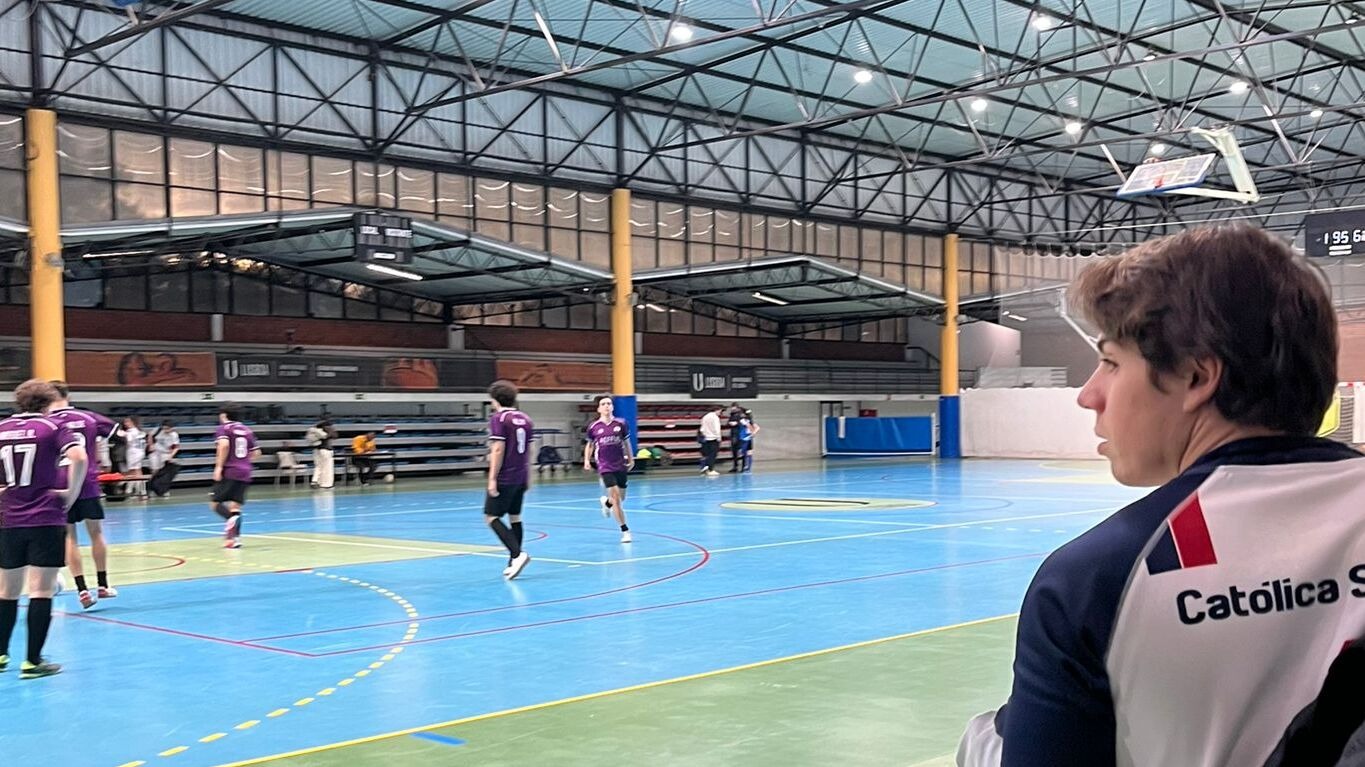 Jogador da Católica observa os seus colegas em ação num treino de futsal.