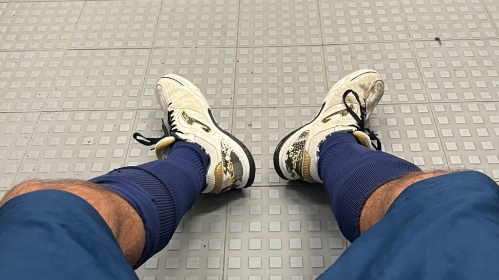 Pernas do jogador da Católica equipado com chuteiras brancas e meias azuis.