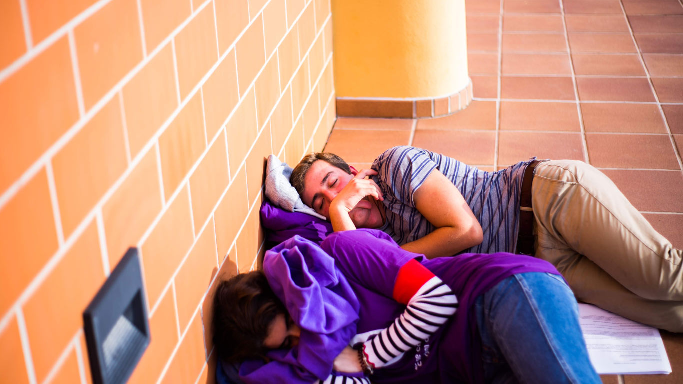 Dois jovens a dormir no chao de tijolo com a cara tapada com camisolas