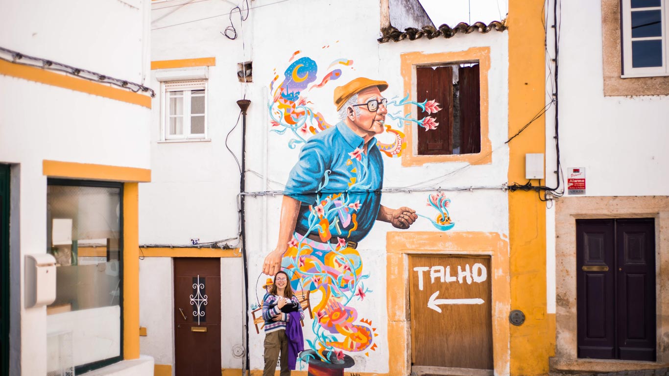 Uma rapariga pousando à frente de uma parede branca e amarela com um desenho de um senhor a andar muito colorido