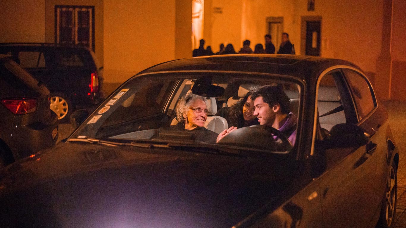 Dois jovens e uma senhora mais velha num carro preto a sorrir