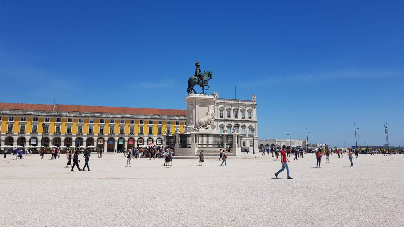 Estátua de D. José na Praça do Comércio. Os turistas passeiam na praça e aproveitam o sol.