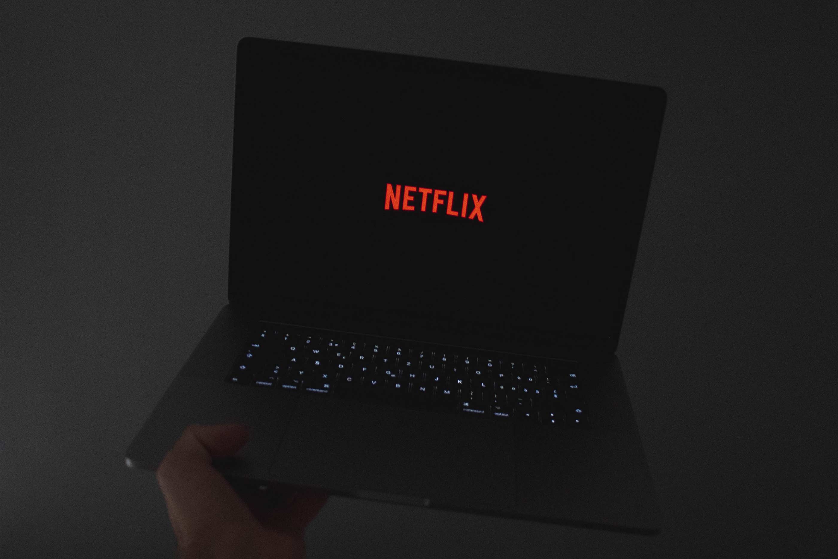 Mão a segurar o computador com o logótipo da Netflix.