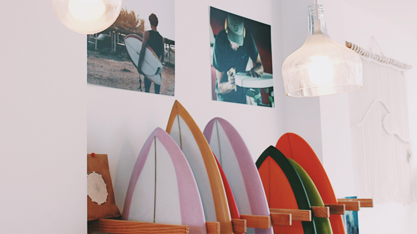 Várias pranchas de surf coloridas ao pé de uma parede com fotografias.