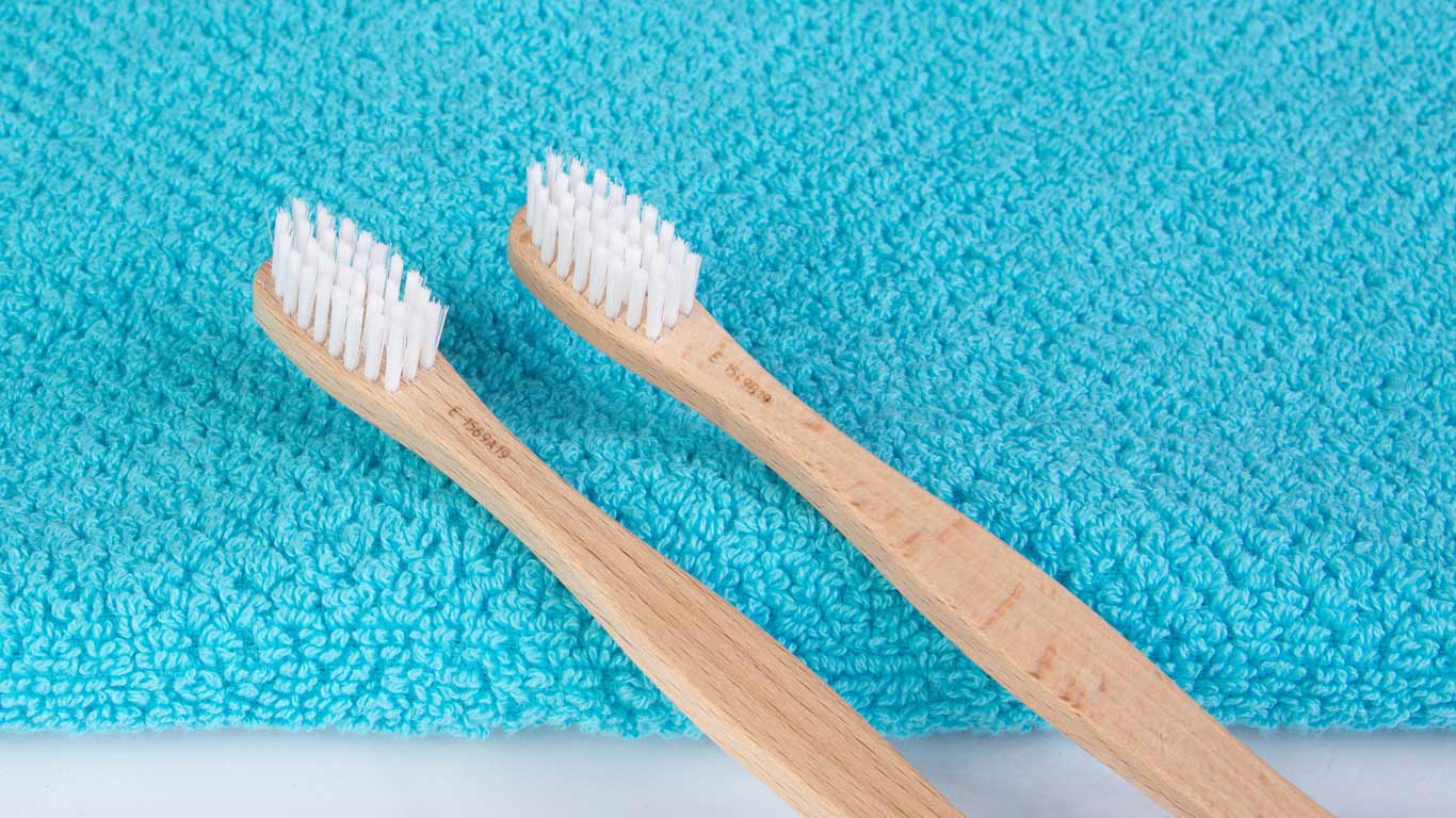 Duas escovas de dentes feitas de bambu em cima de um pano azul.