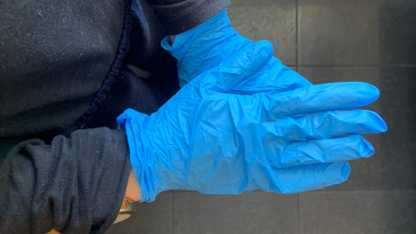 Pessoa a utilizar luvas descartáveis azuis nas mãos