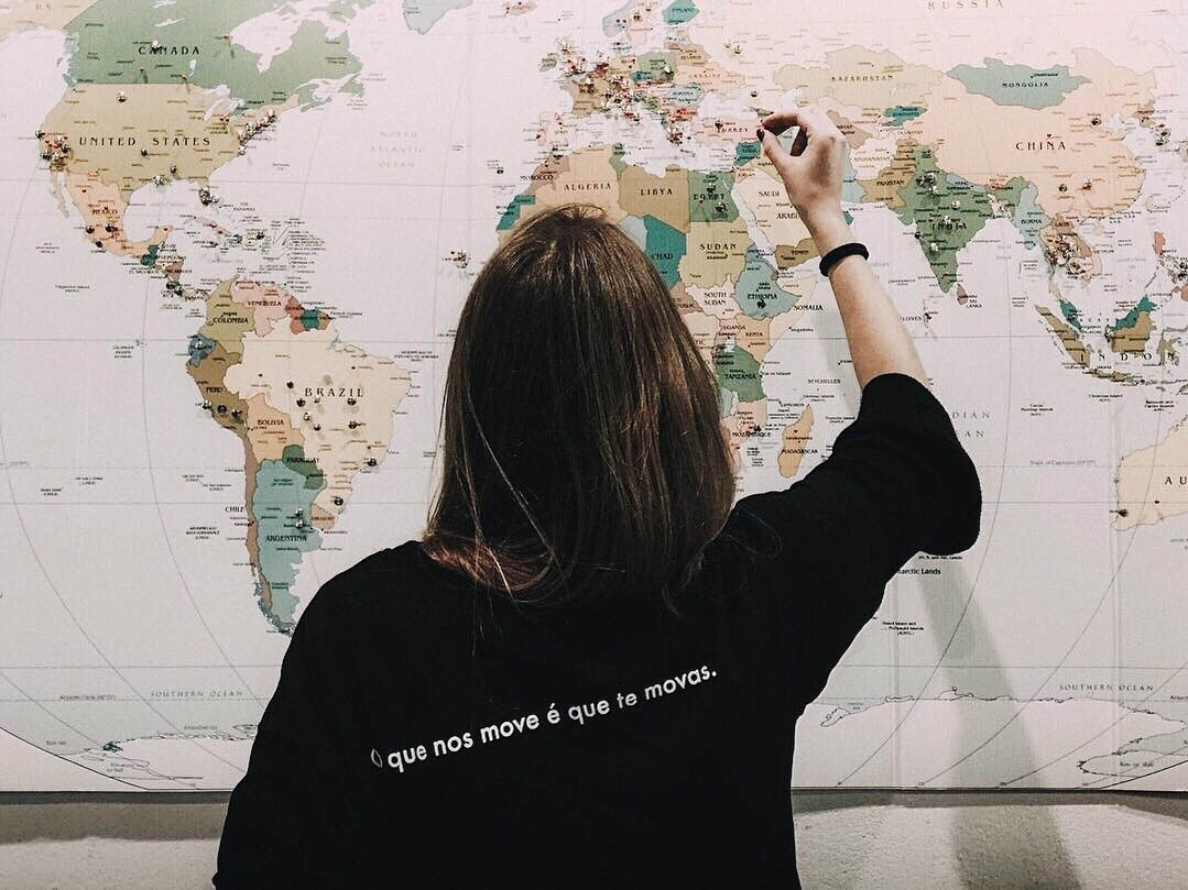 Rapariga com T-shirt preta de costas com mapa mundo de fundo