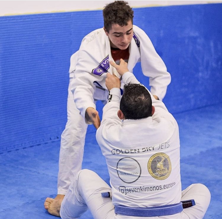 Dois praticantes de jiu-jitsu de idades distintas numa posição de jiu-jitsu denominada de guarda aberta.