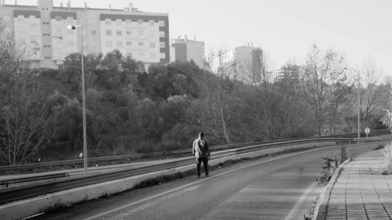 Fotografia a preto e branco de homem a andar na estrada. Uma das 80 fotografias da exposição "Ballad Of Today"