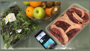 Telemovél com a app da To Good to Go em cima da mesa com a comida recolhida, entre ela carne, alface e frutas