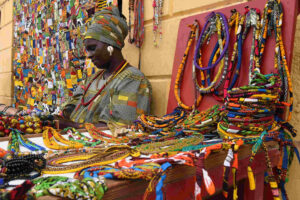 Uma comerciante senegalesa de vestes coloridas na sua banca de venda de artesanato e produtos de bijuteria