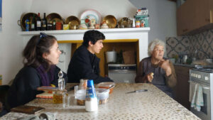 Missionários do Movimento ao Serviço da Vida na casa de uma idosa, sentados e a conversarem na cozinha