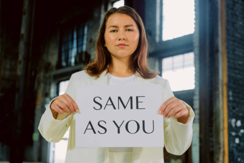 Uma mulher adulta a segurar um cartaz que diz "Same As You"