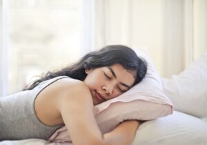 Mulher com cabelo castanho e pijama cinzento a dormir à claridade agarrada