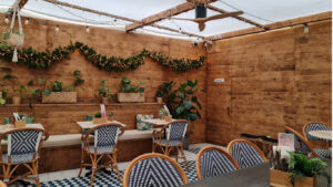 Espaço do restaurante composto por cadeiras de estilo parisiense com pormenores azuis e brancos. O espaço conta ainda com paredes de madeira e várias plantas.