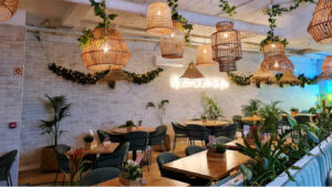 Espaço de restaurante marcado por uma enorme quantidade de candeeiros de verga. Este espaço é também composto por mesas de madeira, cadeiras verdes e várias plantas.